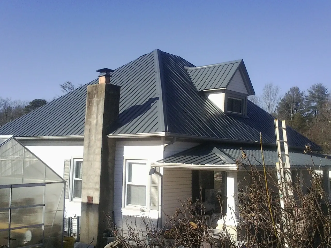 Dark blue standing seam metal roof on a white farmhouse with dormer — Slate & Tile Roof Repair by Roofing Brothers in Greenwood