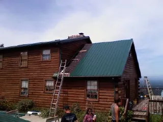 Green metal roof going on a two story log home with ladders set in Greenwood